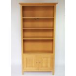 A modern light oak bookcase, with adjustable shelves, above two cupboard doors,