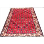 A hand woven wool rug, worked with a repeating geometric pattern against a red ground,