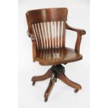 An Edwardian oak office swivel desk chair, with bar back and solid seat,