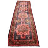A Caucasian hand woven wool runner, worked with four hooked medallions against a red ground,
