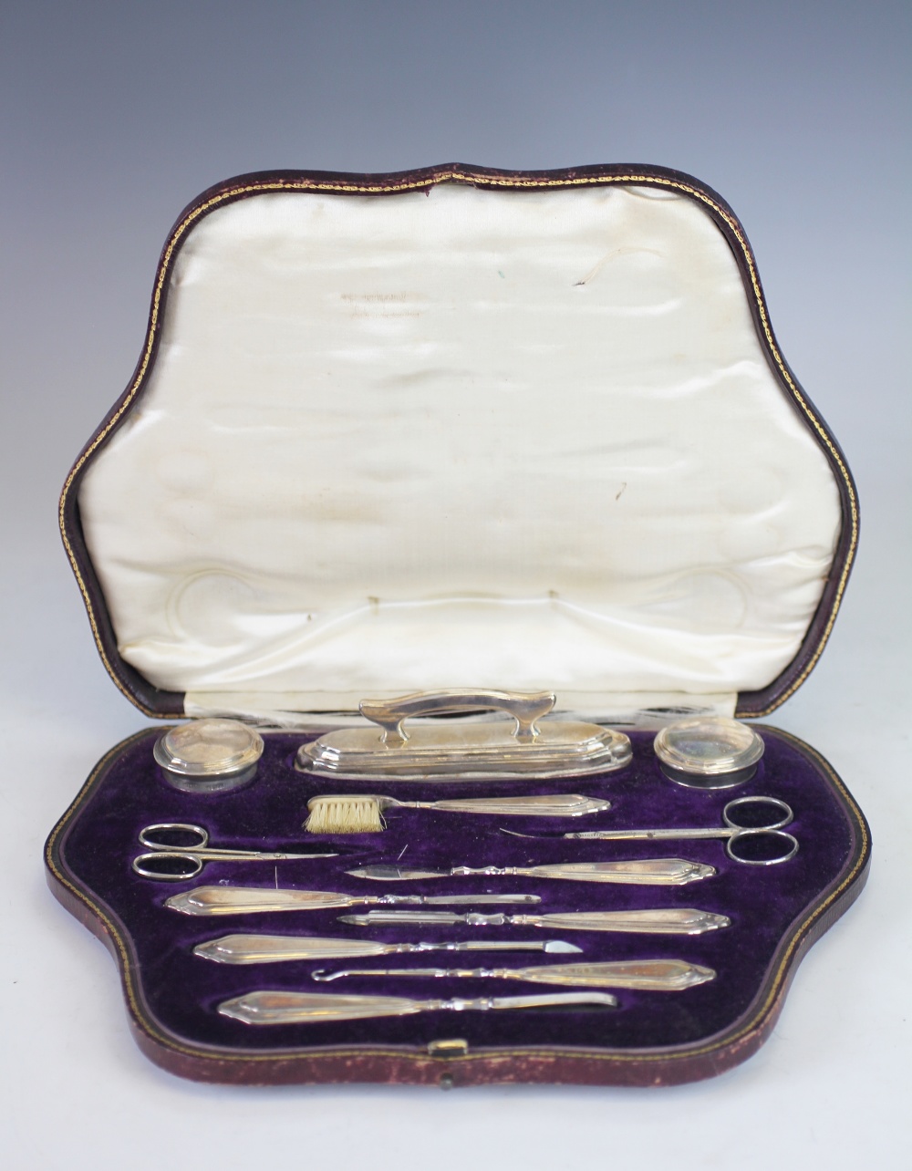 A cased silver manicure set, 'CD' London 1916, comprising; buffers, jars, tools, scissors,