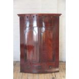 A late George III mahogany bow front hanging corner cabinet, with two arched panel doors,