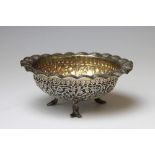 An Indian white metal circular bowl, with flared rim and foliate detailing, on entwined fish feet,