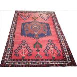 A Caucasian wool rug, worked with a geometric blue medallion against a red ground,