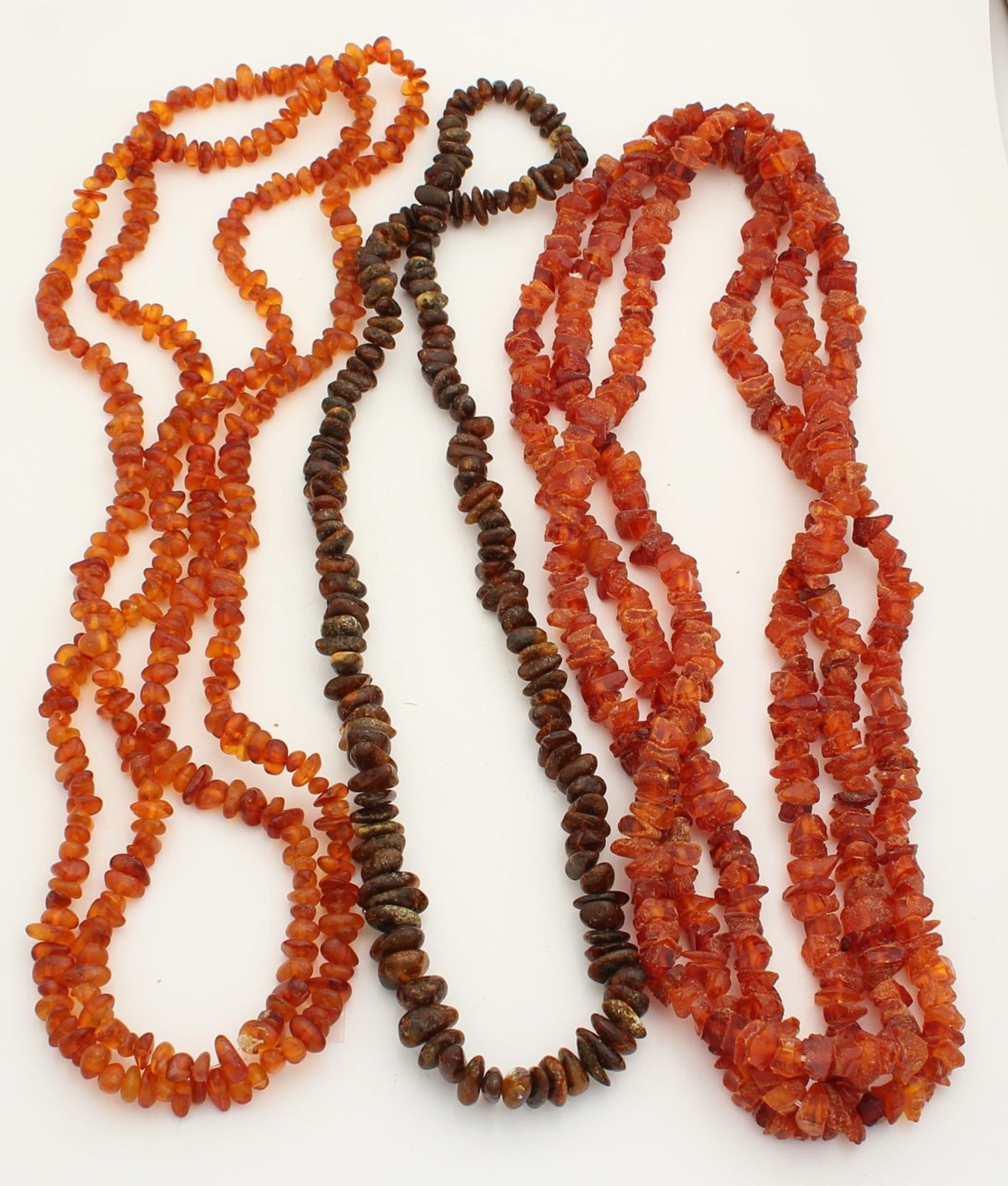 Three long cords with amber beads, raw or only tumbled. One with a dark color. Size approximately