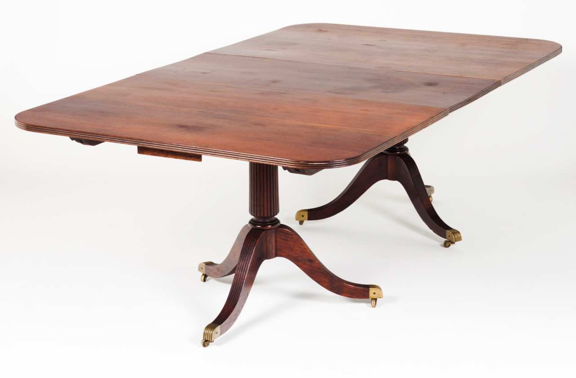 An English dining table Mahogany Top above two fluted columns ending in three curved legs with