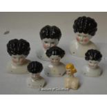 Seven glazed porcelain dolls heads, six of which have black curly hair, painted blue eyes and rosy