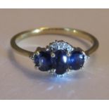 An 18ct gold sapphire and diamond three-stone ring. Size n. The slightly graduated oval-shape