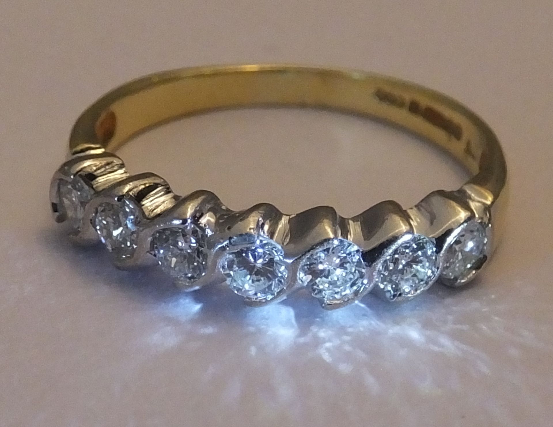 An 18ct gold diamond seven-stone ring. Each brilliant-cut diamond, within a curved spacer, to the