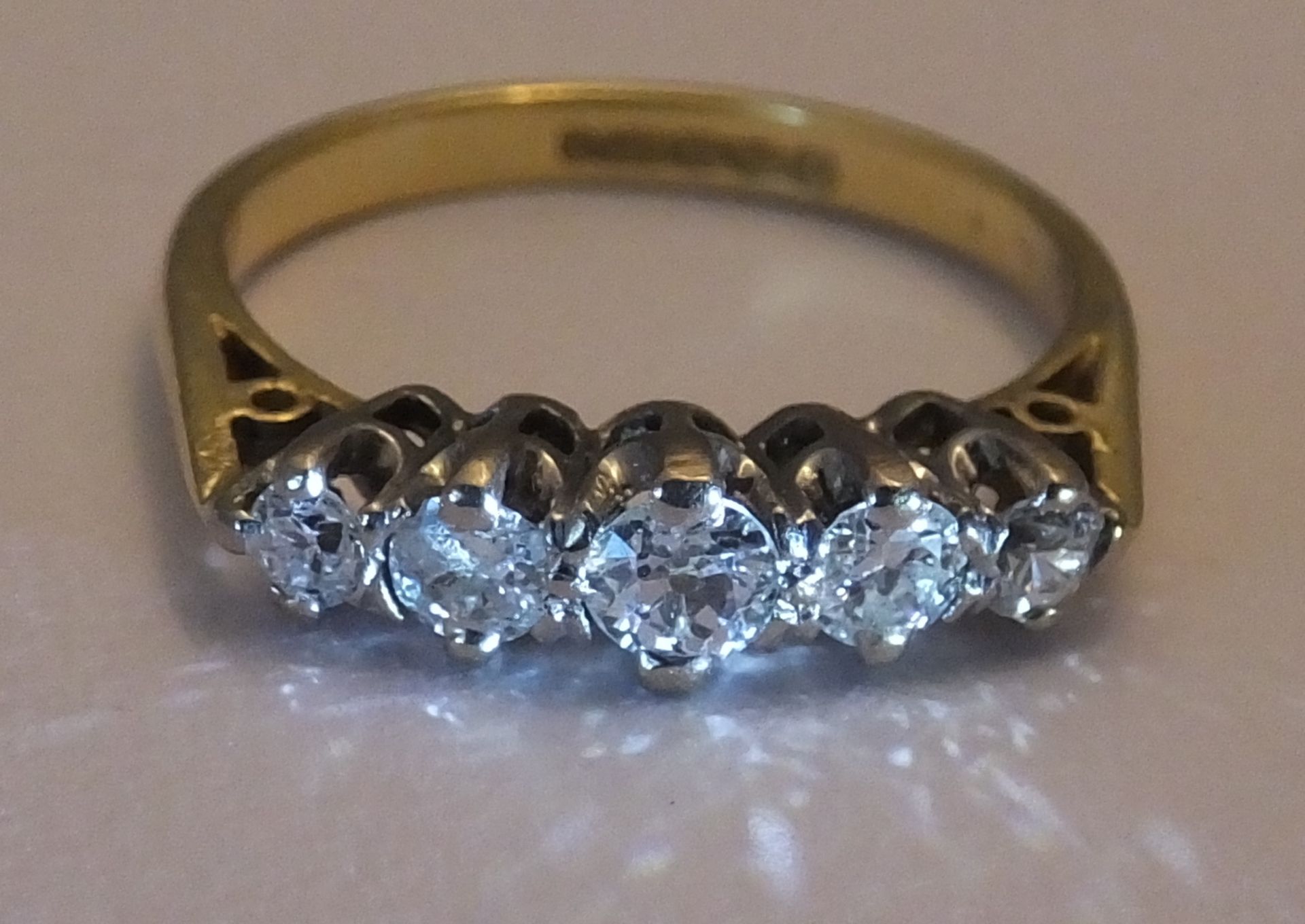 An 18ct gold diamond five-stone ring. Size J. The graduated old-cut diamond line, to the tapered