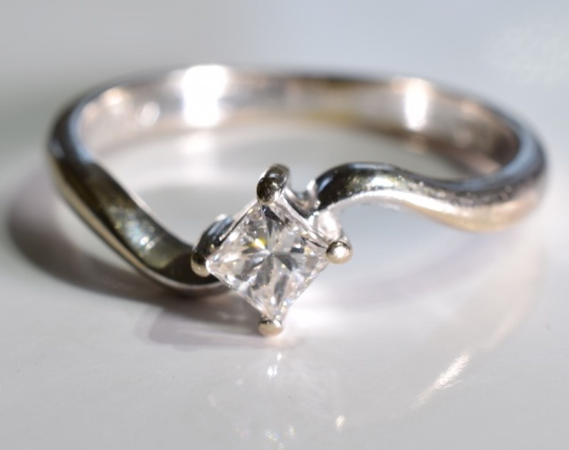 A diamond single-stone crossover ring. The _ square-shape diamond, to the asymmetric shoulders and