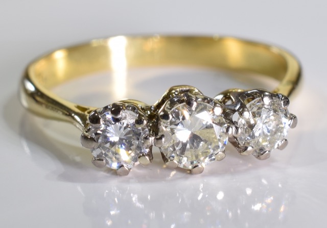 A diamond three-stone ring. The graduated brilliant-cut diamond line, to the tapered shoulders and