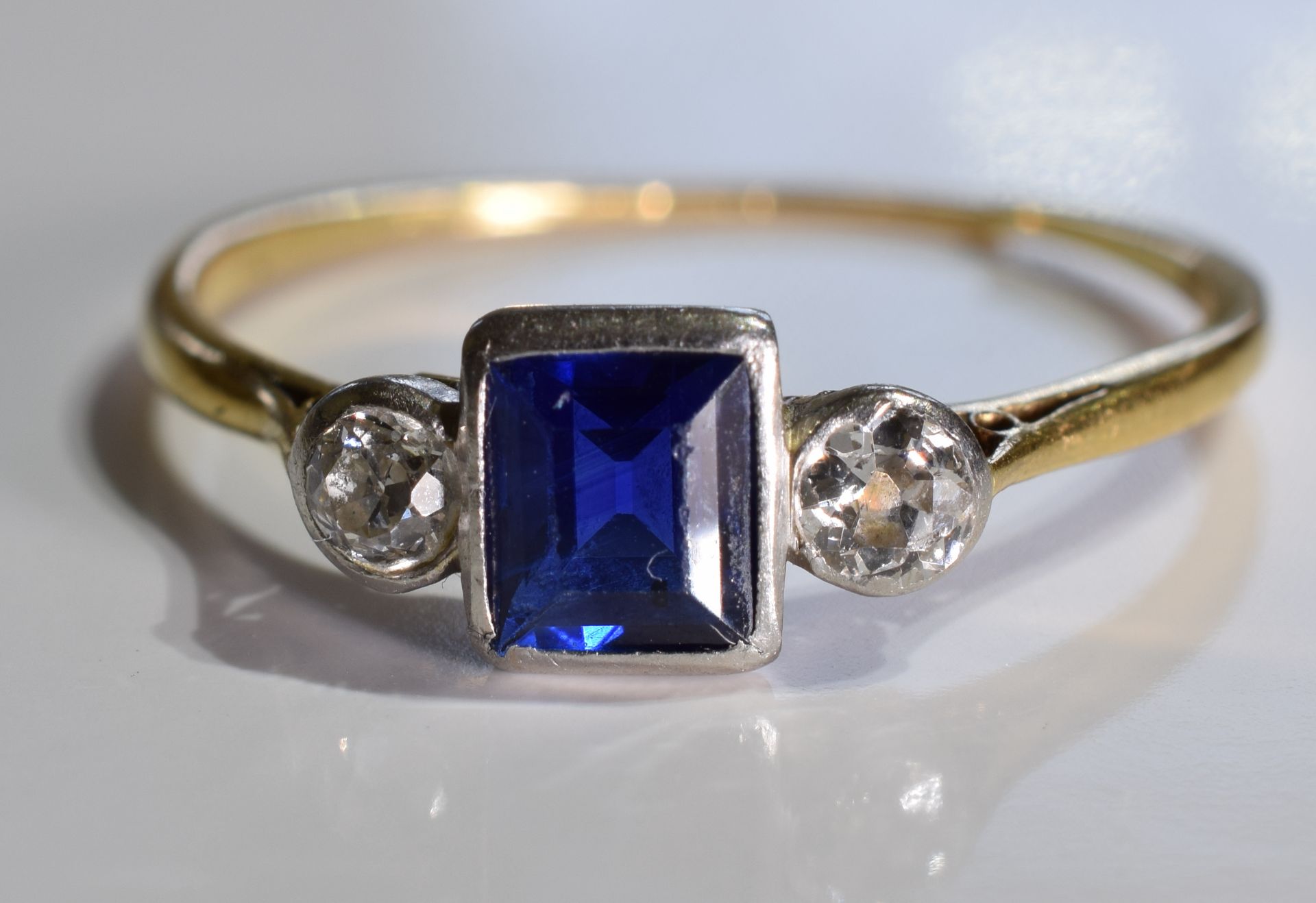 A sapphire and diamond ring. The square-shape sapphire with old-cut diamond sides to the tapered