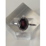 White gold ladies ring set with an oval garnet and diamond surroundWhite gold ladies ring set with