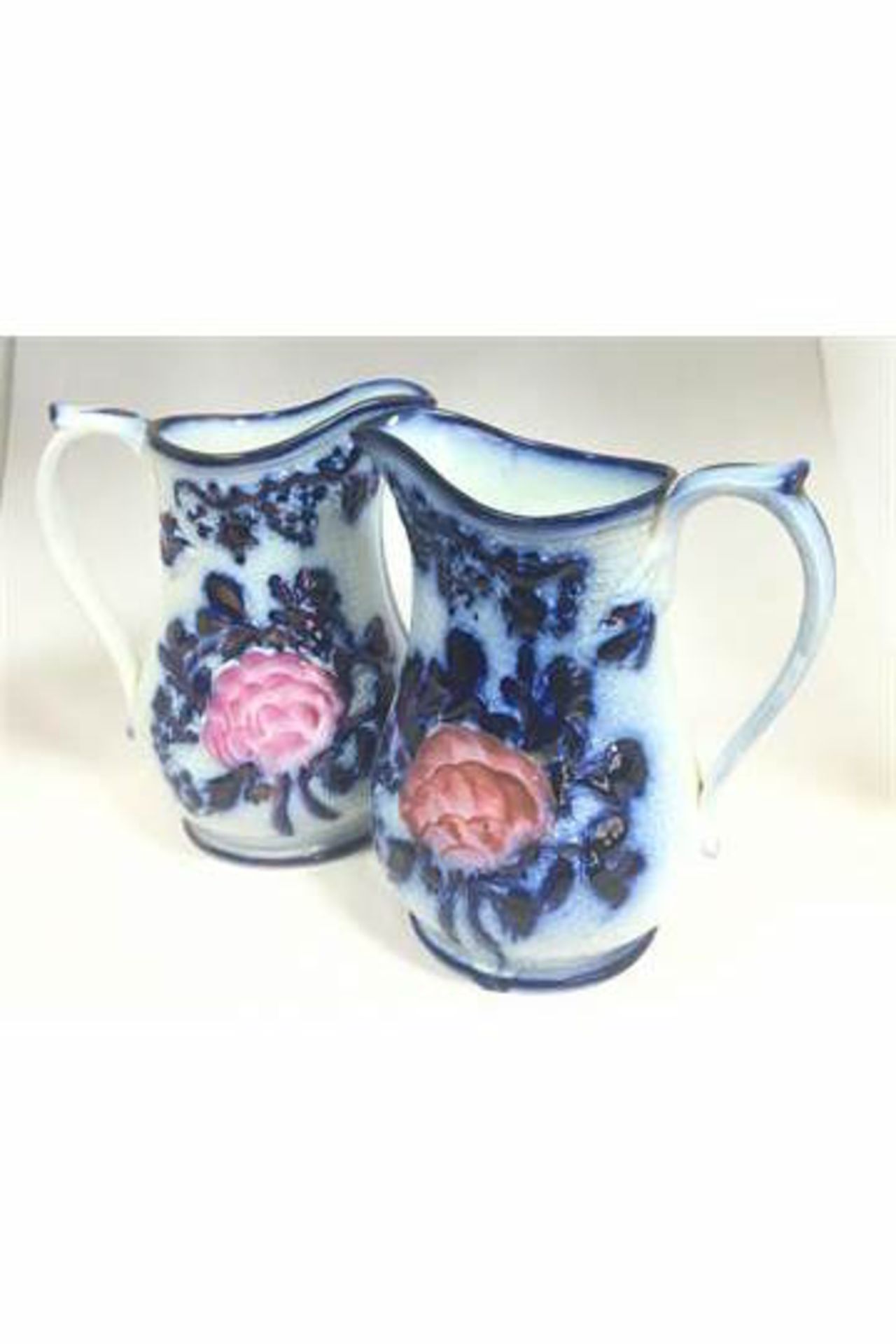 A PAIR OF 19TH CENTURY RELIEF MOULDED FLOW BLUE PITCHERS OR JUGS, HANDPAINTED WITH PINK FLOWER.