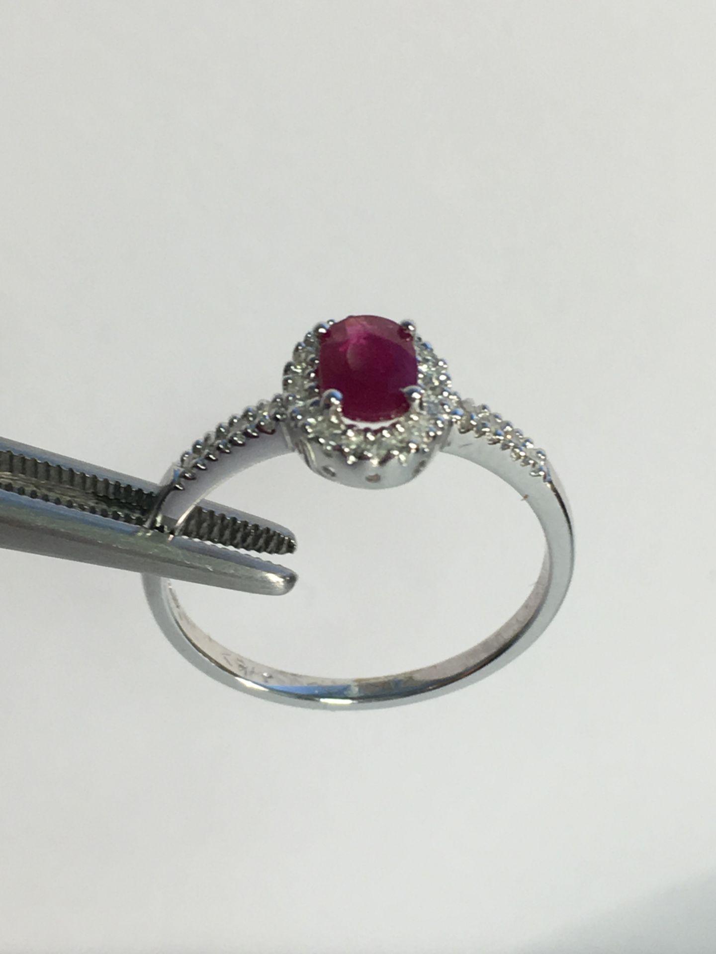 9k White gold ladies ring set with an oval Ruby and diamond surround