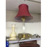 Lamp with glass column leading onto brass top and bottom with a red shade.