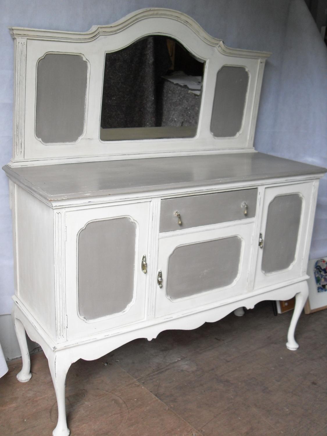 An early 20th century cream-painted sideboard with tray-back domed mirror, central napery drawer and