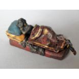 A novelty cold painted bronze figure of a lady reclining on a couch and covered by a removable throw