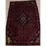 A Persian hand-knotted Hamadan burgundy-ground wool rug with central lozenge-shaped feature and