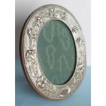 An Edwardian oval silver photos frame with embossed trailing lilies on wooden easel stand by William