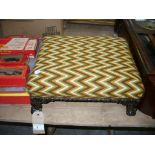 A 19th Century upholstered footstool raised on four heavily carved supports and scroll toes.