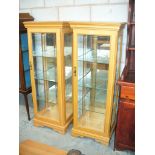 A pair of modern beech wood pedestal display cabinets each with three enclosed glass shelves and a
