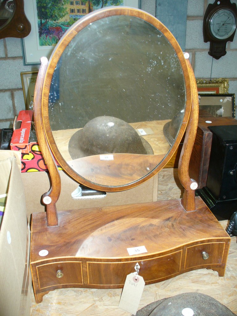 A 19th Century mahogany oval dressing table mirror on a three drawer serpentine plinth.