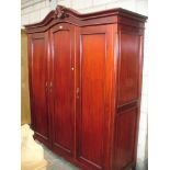 A French style stained wood triple wardrobe with a scrolling leaf carved pediment above three