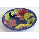 A Walter Moorcroft pottery circular bowl Decorated in the Hibiscus pattern on a blue ground,