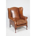A Mid 20th Century tan leather fireside armchair The wingback above padded scroll arms and a loose