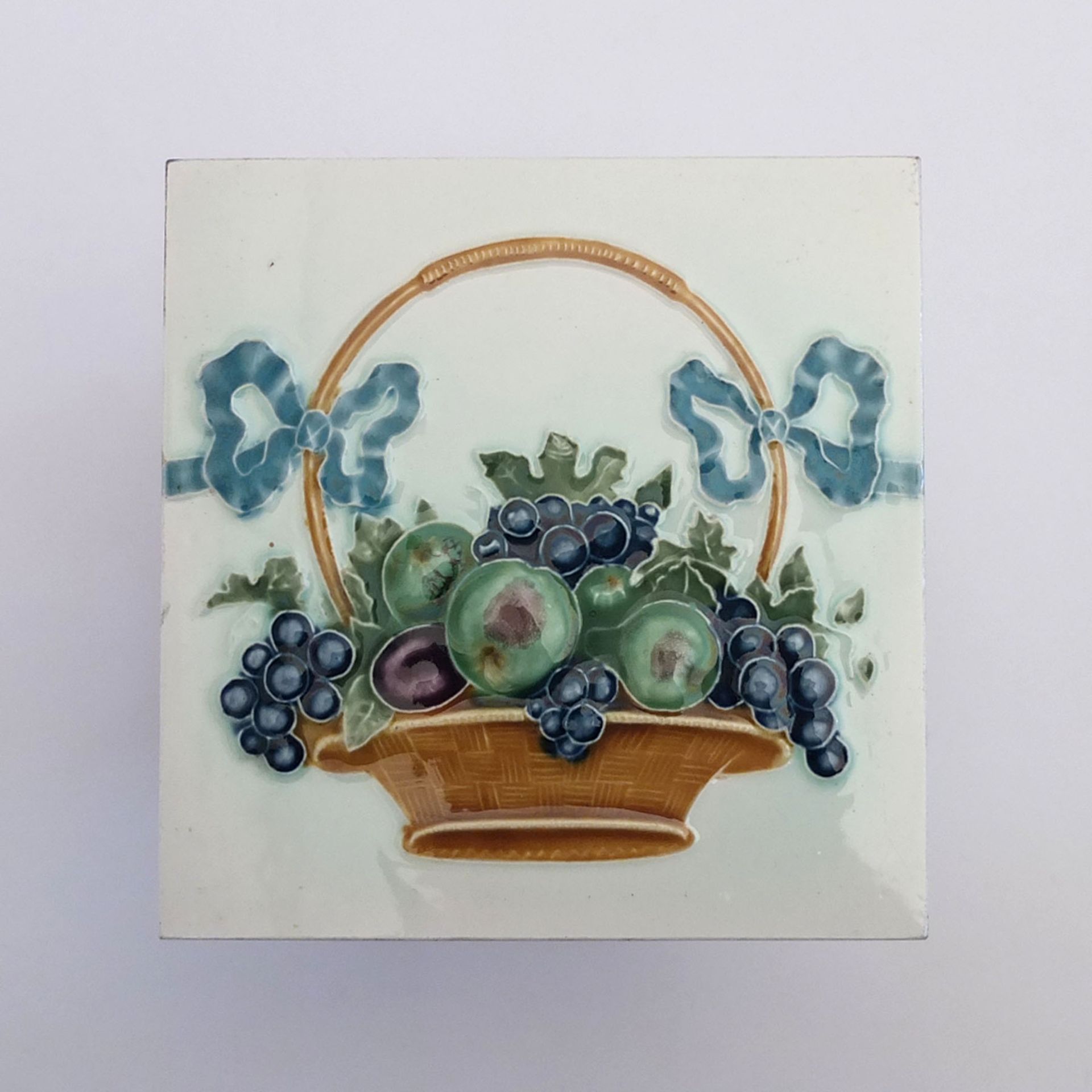 RELIEFFLIESE, Art Jugendstil, Keramik, polychrom, Fruchtkorb mit Schleifen, je 15,1 x 15,1 cm