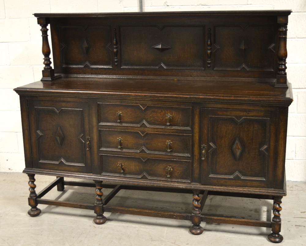 A 1920s oak sideboard with a carved panel and upstand supported by two turned columns,