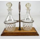 An Edwardian oak and electroplated stand with a pair of clear glass bottle shaped decanters with