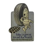 A vintage Michelin hardboard advertising sign depicting Mr Bibendum beside a large Michelin tyre