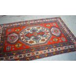 A 20th century Persian style rug with geometric designs against a red ground, fringed edge,