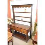 An oak dresser of small proportions with open four shelf plate rack above three drawers and square