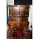 A reproduction oak dresser with plate rack above three drawers and doors, width 139cm.