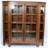 A large pitch pine display cabinet, the twin glazed doors with angled sides raised on tile supports,