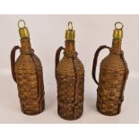 Three cane covered wine bottles with brass covered stoppers and leather straps and handles,