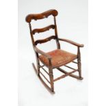 A small late 19th century simulated rosewood rocking chair with carved ladder back and outswept