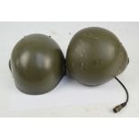 Two 1980s military helmets, one with integral ear protectors and microphone.
