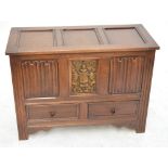 A reproduction oak coffer with hinged lid above central carved panel bearing a crest with mythical