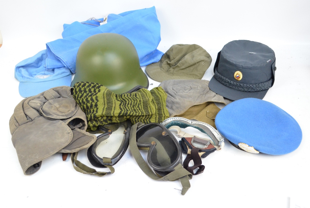 A reproduction German helmet, a peaked cap, various soft caps and goggles.