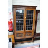 A 1920s oak and lead glazed display cabinet with twin panelled lower doors,