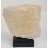 A fragment of Egyptian hieroglyphs carved in sandstone, mounted on a square section plinth,