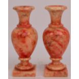 A pair of decorative polished red/orange marble baluster vases with flared rims raised on spreading