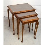 A nest of three glass-topped walnut tables.