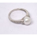 An 18ct white gold ring with central cultured pearl surrounded by melee diamonds to shoulders,