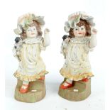 A pair of large bisque porcelain figures of girls in bonnets holding a puppy,